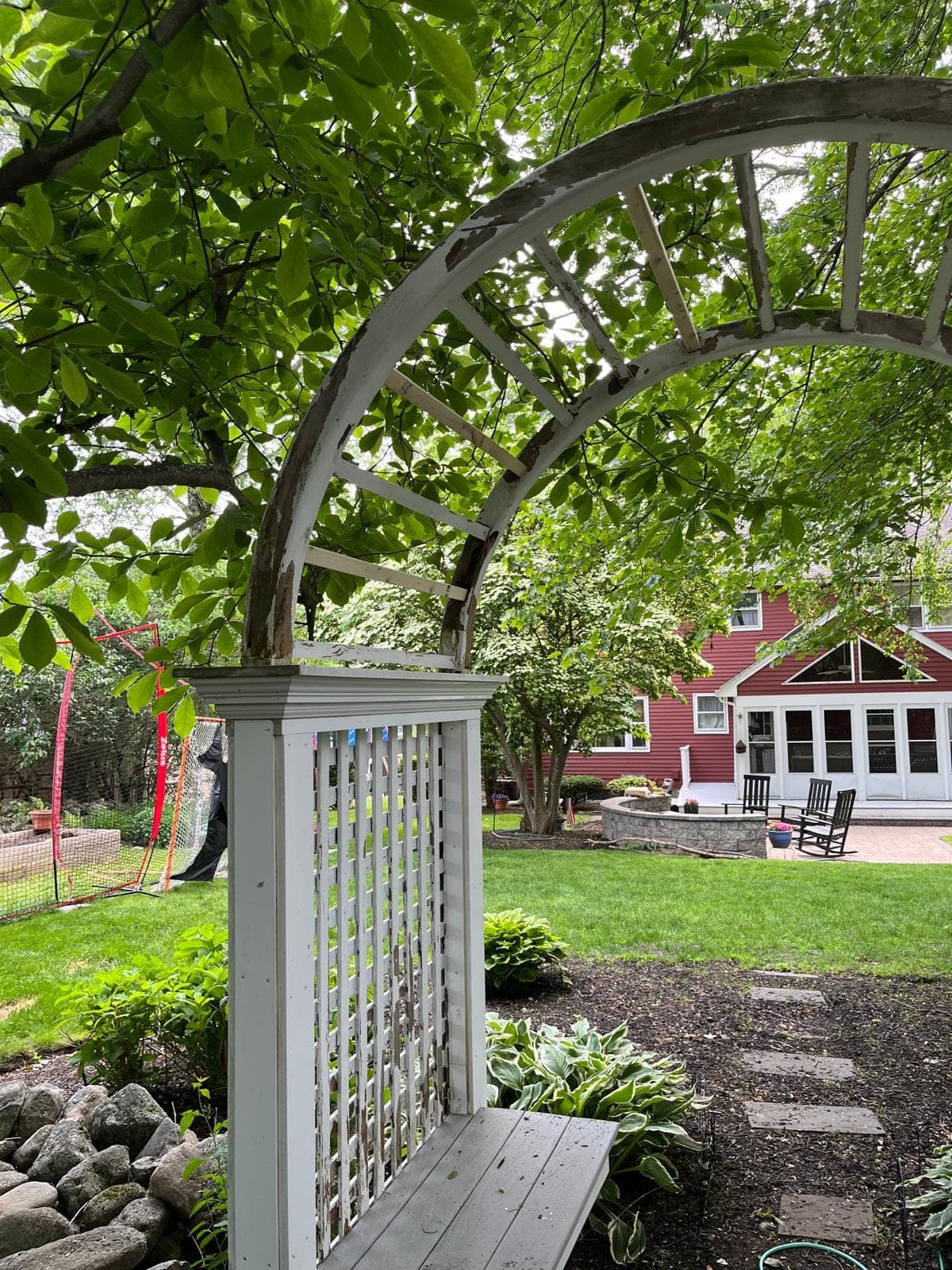 A wooden garden arbour with new lattice posts framing a red house across a lawn