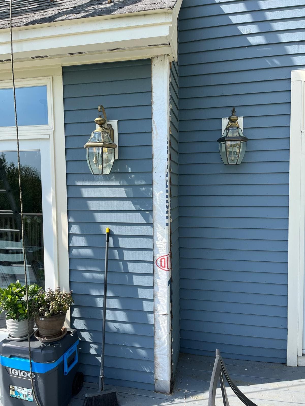 Two brass lanterns either side of a doorway on a blue clapboard wall with a new primed corner board