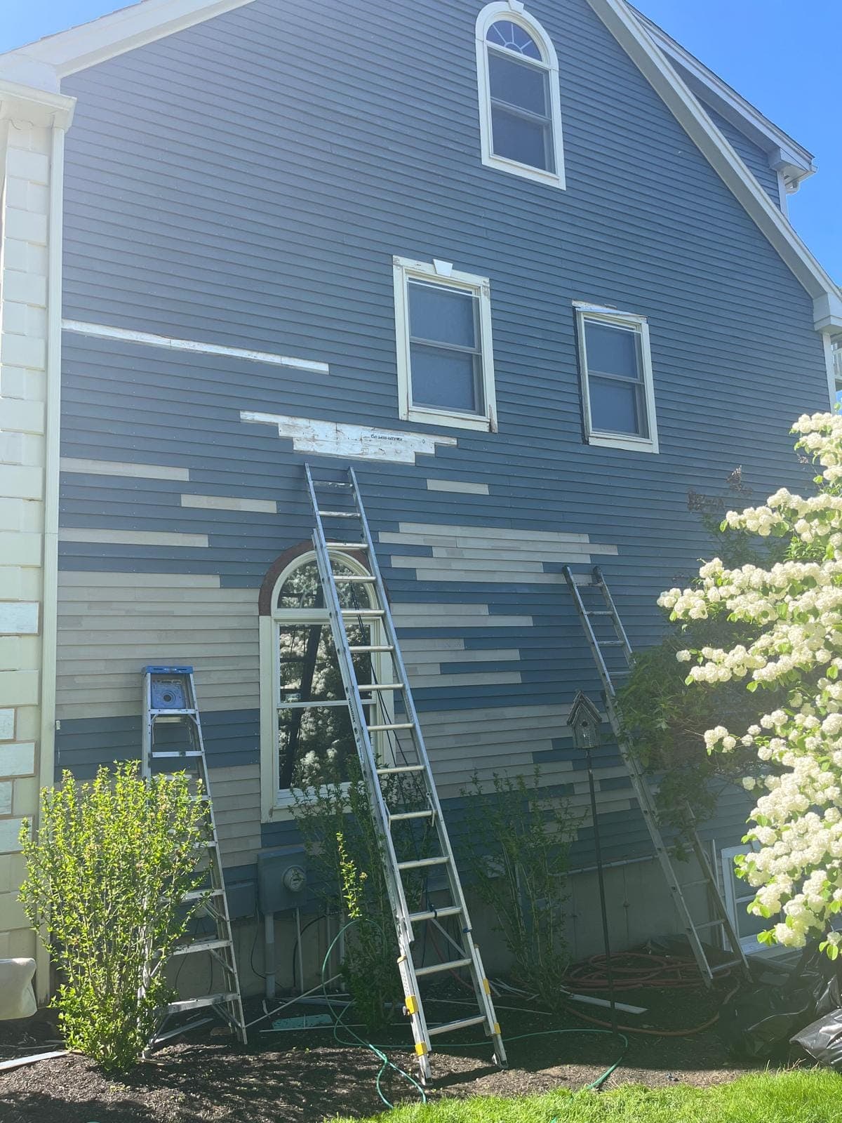 New primed clapboard runs stepping across a blue wall beside an arched window