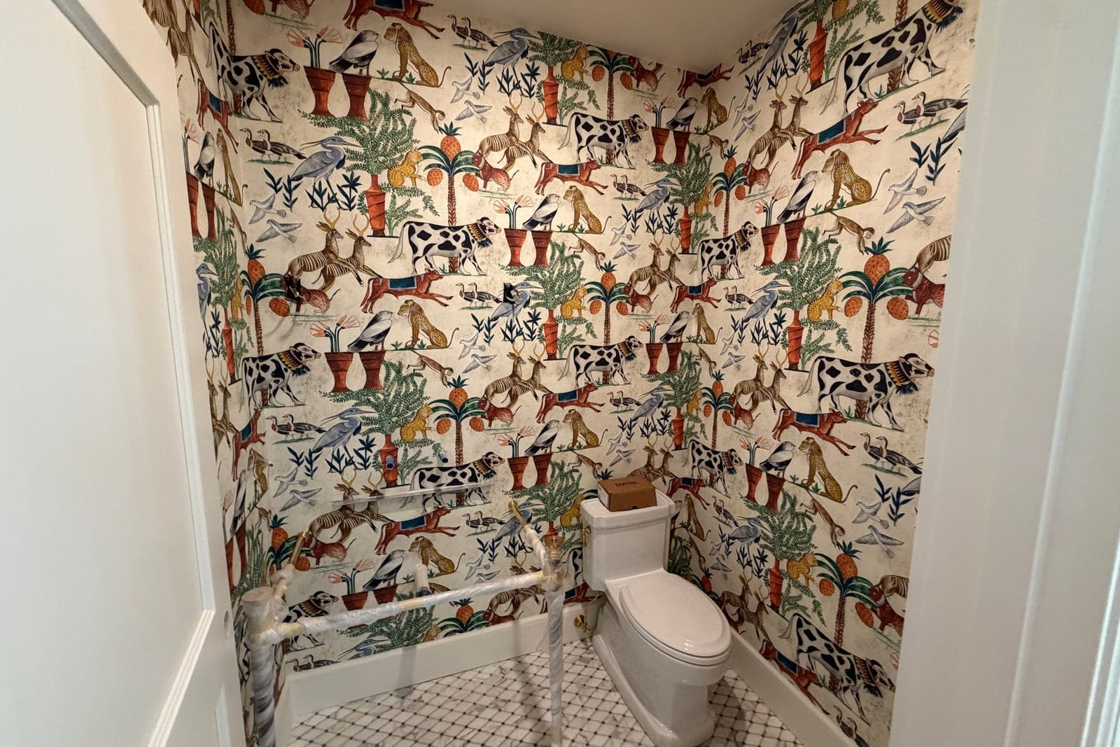 Powder room mid-install: Egyptian animal print paper on all three walls, the toilet supply lines still wrapped in plastic